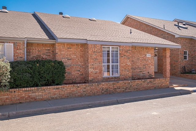 view of side of property with brick siding and roof with shingles