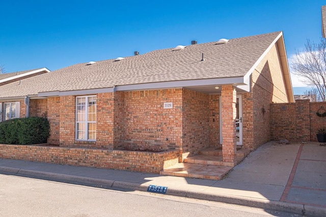 exterior space featuring a patio area, roof with shingles, and brick siding