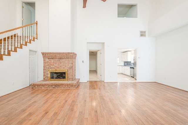 unfurnished living room featuring baseboards, visible vents, a ceiling fan, light wood-type flooring, and a brick fireplace