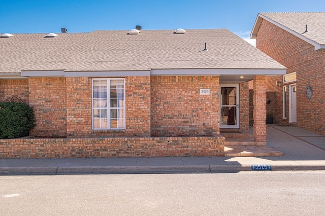 exterior space with brick siding and roof with shingles