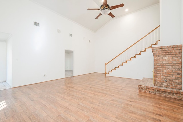 unfurnished living room with light wood finished floors, visible vents, ornamental molding, a ceiling fan, and high vaulted ceiling