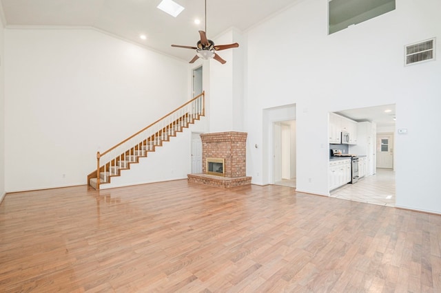 unfurnished living room featuring a fireplace, a ceiling fan, visible vents, light wood-style floors, and crown molding