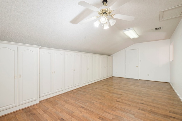 additional living space featuring a textured ceiling, vaulted ceiling, light wood-type flooring, and visible vents