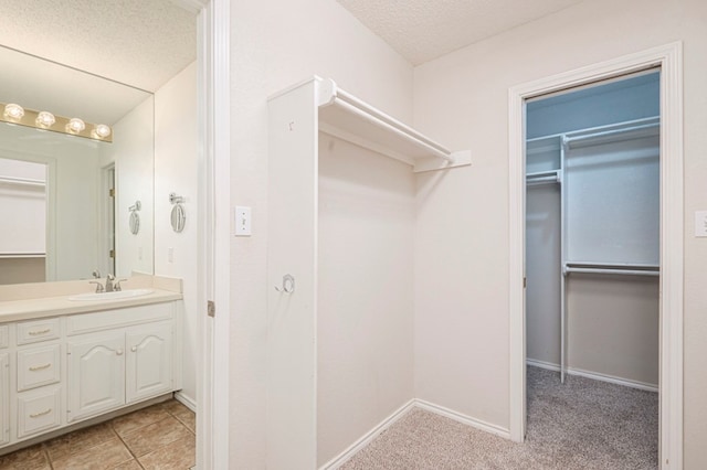 bathroom featuring a textured ceiling, tile patterned flooring, vanity, baseboards, and a spacious closet