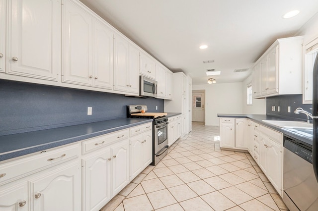 kitchen featuring light tile patterned floors, stainless steel appliances, dark countertops, white cabinets, and a sink