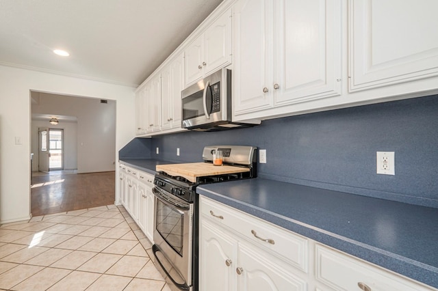 kitchen featuring dark countertops, decorative backsplash, appliances with stainless steel finishes, white cabinetry, and light tile patterned flooring