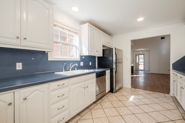 kitchen featuring light tile patterned floors, stainless steel appliances, dark countertops, white cabinets, and a sink