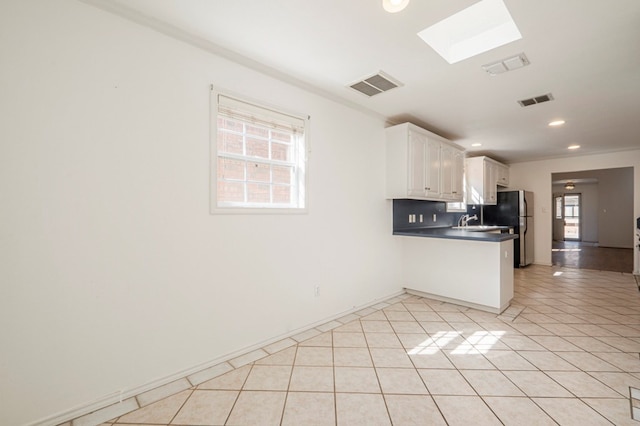 kitchen featuring light tile patterned floors, visible vents, white cabinetry, freestanding refrigerator, and dark countertops