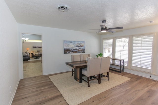 dining space with a textured ceiling, ceiling fan with notable chandelier, and hardwood / wood-style flooring