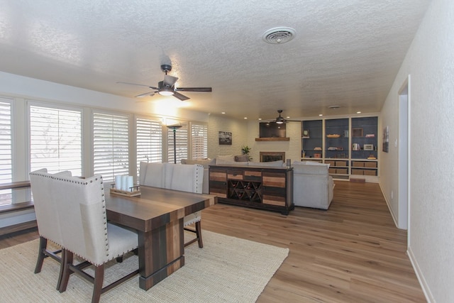 dining space with a textured ceiling, ceiling fan, wood-type flooring, and a fireplace