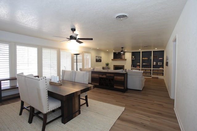 dining room with hardwood / wood-style floors, ceiling fan, a fireplace, and a textured ceiling