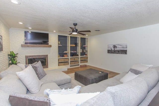 living room with ceiling fan, a fireplace, a textured ceiling, and hardwood / wood-style flooring