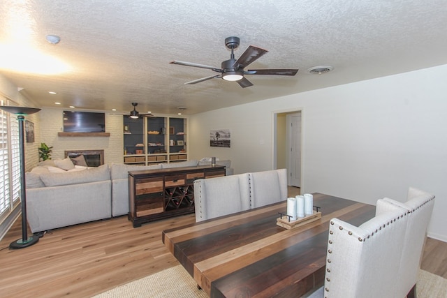 dining space featuring a fireplace, a textured ceiling, light wood-type flooring, and ceiling fan