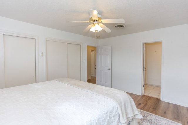 bedroom with a textured ceiling, light hardwood / wood-style flooring, ceiling fan, and multiple closets