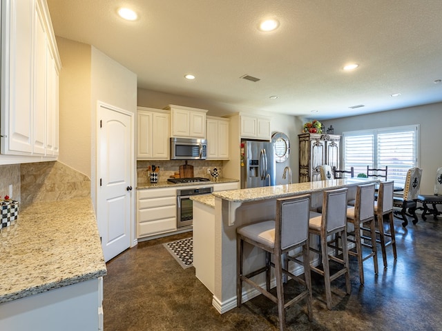 kitchen with white cabinetry, light stone countertops, stainless steel appliances, and a center island