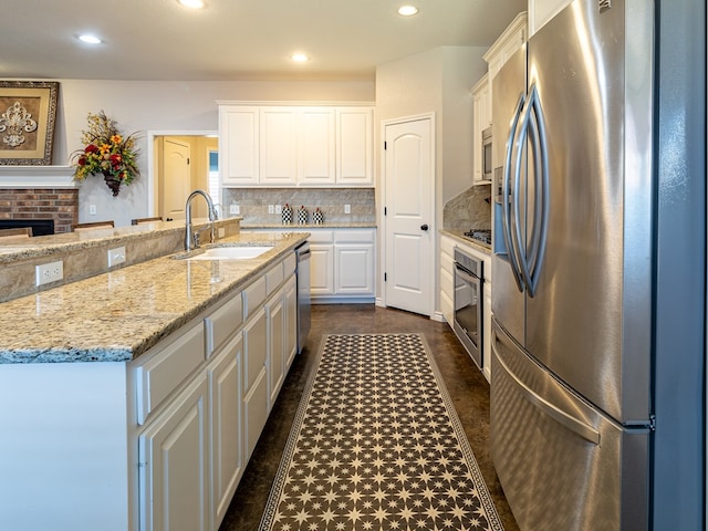 kitchen featuring appliances with stainless steel finishes, sink, white cabinets, light stone countertops, and a spacious island