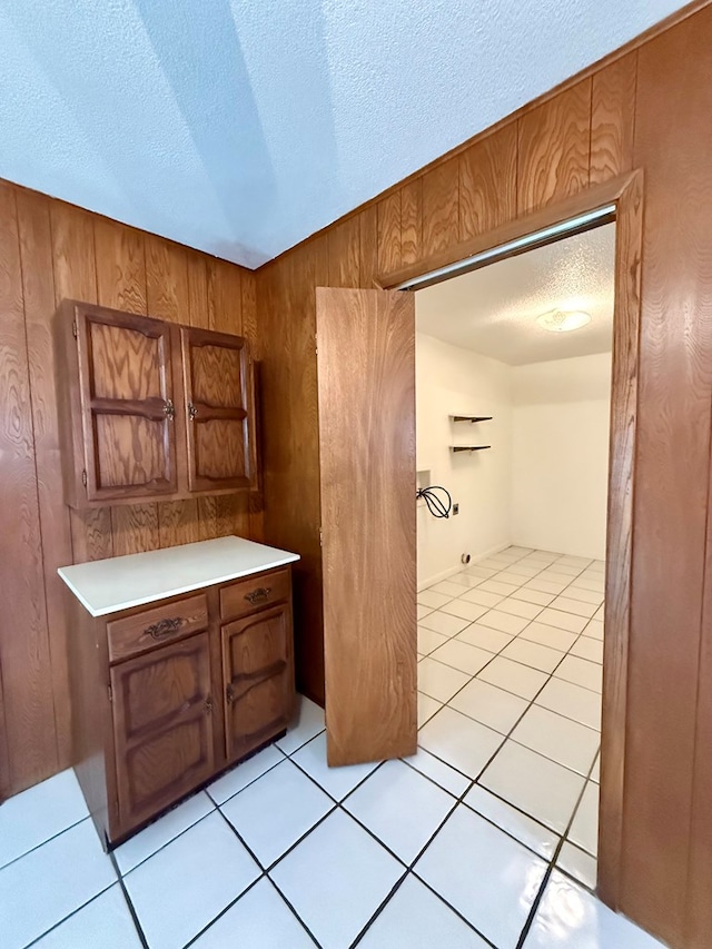 kitchen with wood walls, a textured ceiling, and light tile patterned floors