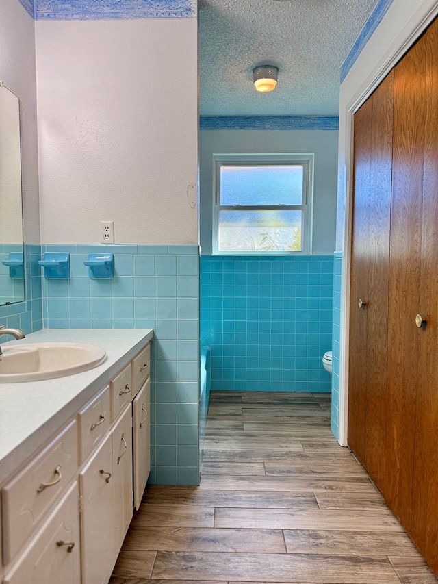 bathroom featuring toilet, a textured ceiling, tile walls, vanity, and hardwood / wood-style flooring