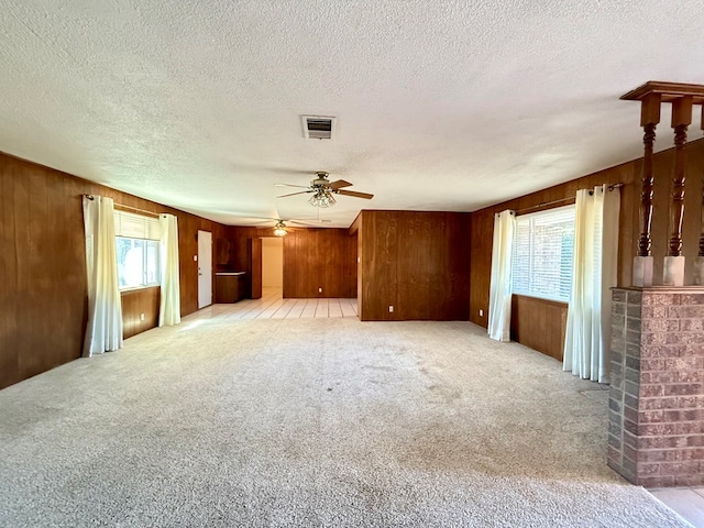 unfurnished living room with ceiling fan, a wealth of natural light, light colored carpet, and wooden walls