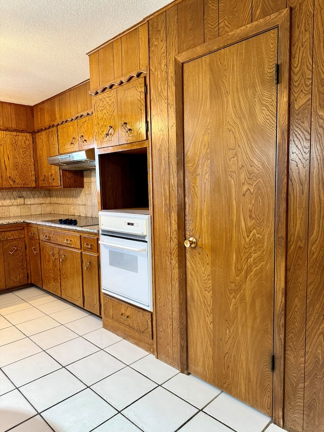 kitchen with light tile patterned floors, backsplash, black electric stovetop, a textured ceiling, and oven