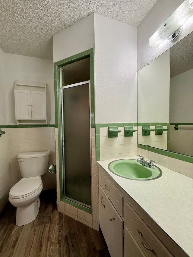 bathroom with hardwood / wood-style floors, an enclosed shower, a textured ceiling, and tile walls