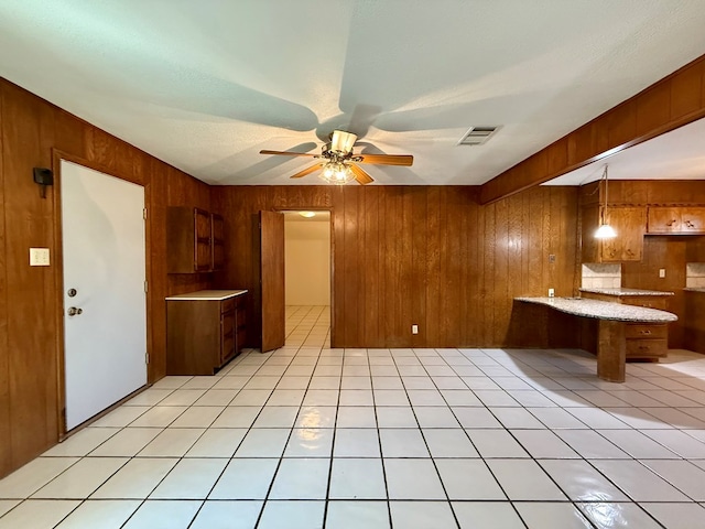 kitchen with light tile patterned flooring, ceiling fan, and wood walls