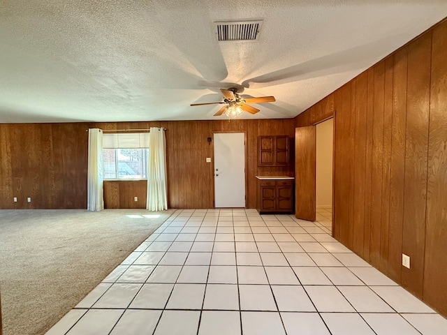 spare room with ceiling fan, light colored carpet, a textured ceiling, and wood walls