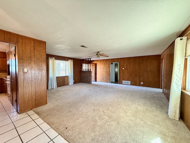 unfurnished living room featuring a textured ceiling, light colored carpet, ceiling fan, and wood walls