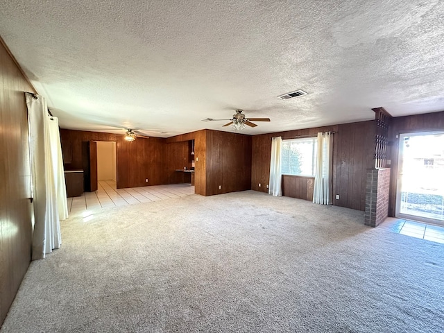 unfurnished living room with ceiling fan, light colored carpet, and wooden walls