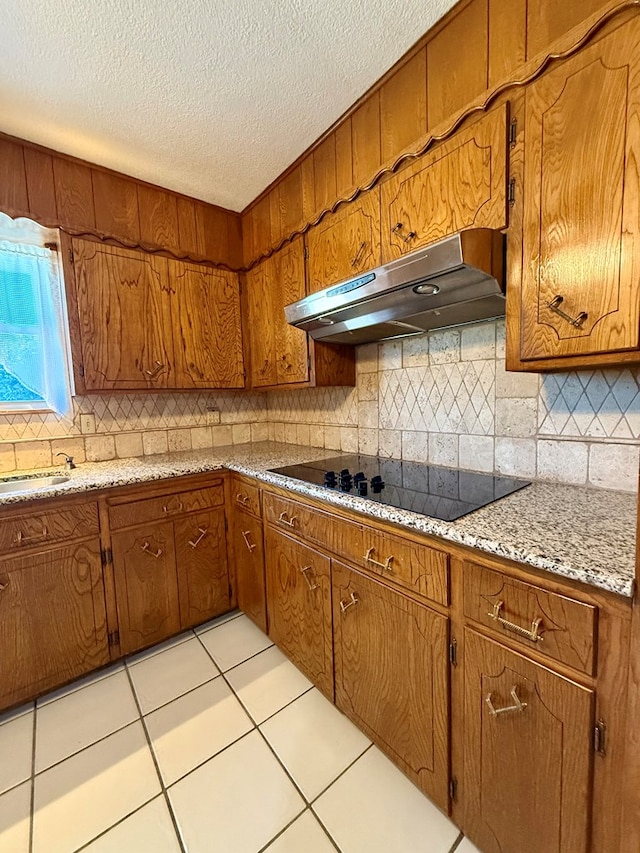 kitchen featuring light tile patterned flooring, black electric stovetop, backsplash, and light stone counters