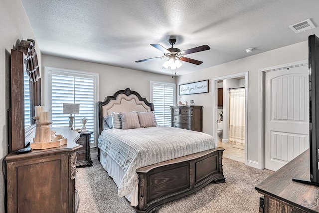 bedroom with ceiling fan, light colored carpet, a textured ceiling, and connected bathroom