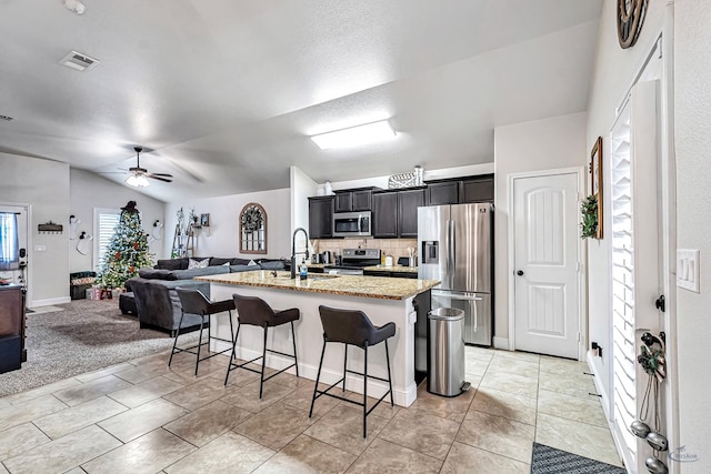 kitchen featuring sink, stainless steel appliances, lofted ceiling, a kitchen bar, and a center island with sink