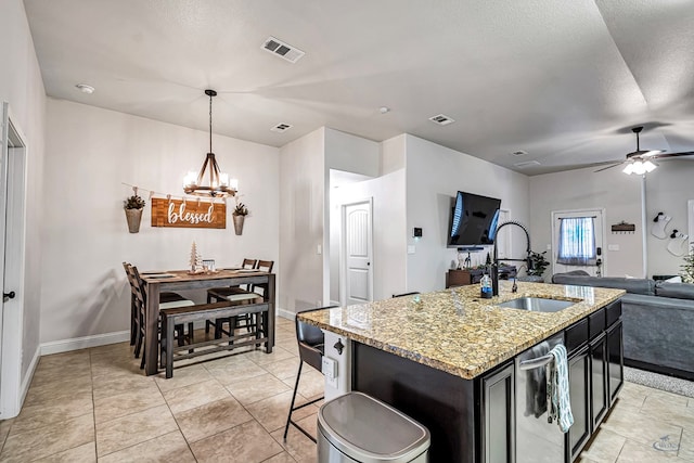 kitchen featuring ceiling fan with notable chandelier, sink, hanging light fixtures, an island with sink, and light stone counters