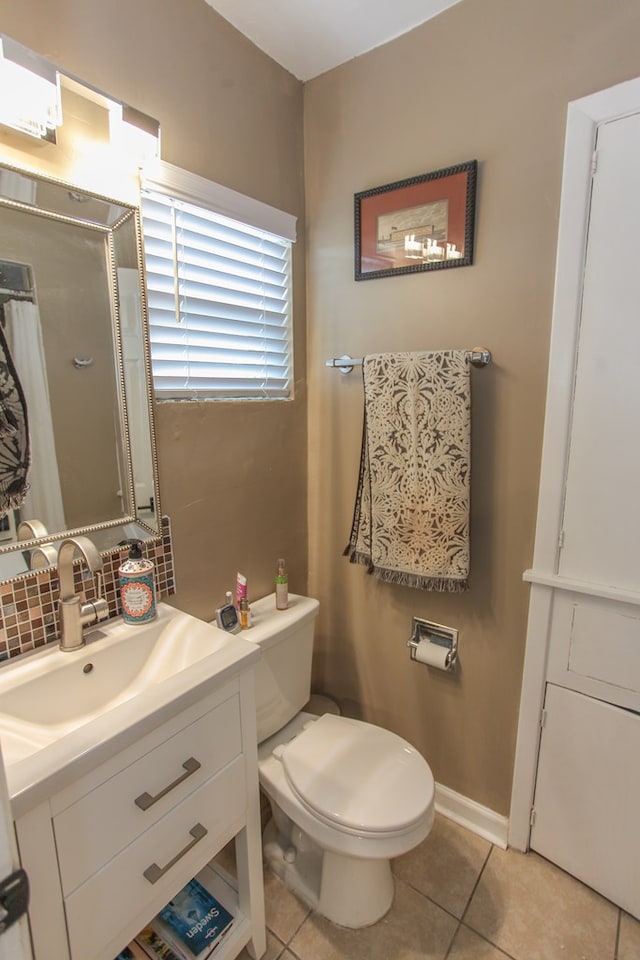 bathroom with tile patterned flooring, toilet, vanity, baseboards, and tasteful backsplash