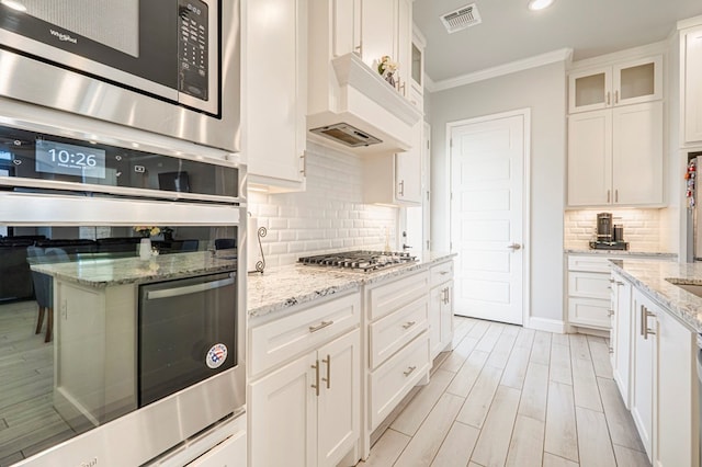 kitchen featuring light stone counters, ornamental molding, stainless steel appliances, and white cabinets