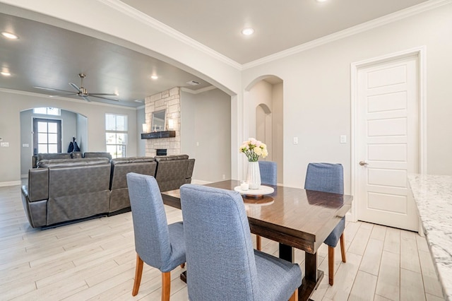 dining room featuring ceiling fan, ornamental molding, a stone fireplace, and light hardwood / wood-style flooring