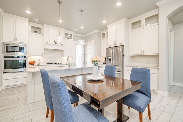 dining space with ornamental molding, sink, and light hardwood / wood-style flooring