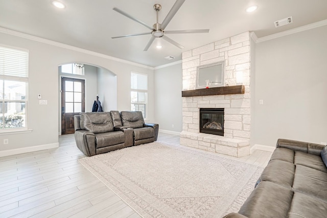 living room featuring crown molding, a fireplace, ceiling fan, and light wood-type flooring