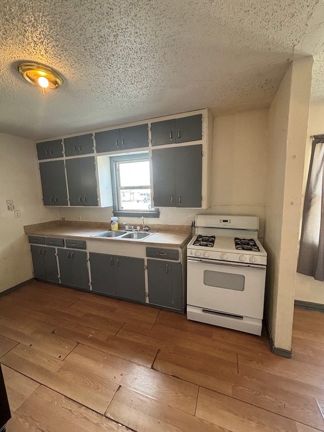kitchen featuring wood-type flooring, a sink, white gas stove, and gray cabinets