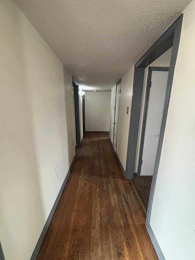 hallway with baseboards, hardwood / wood-style flooring, and a textured ceiling