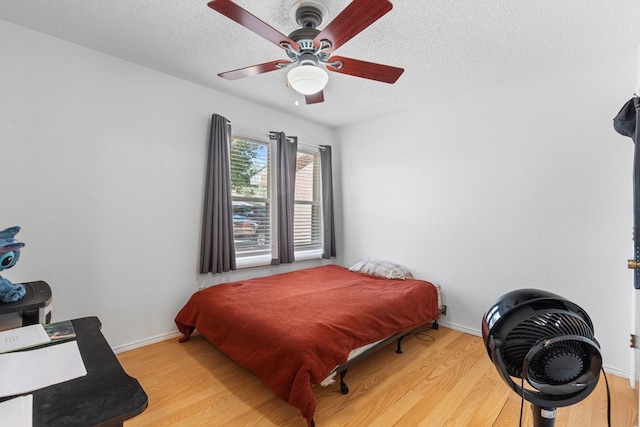 bedroom with light wood-style floors, a textured ceiling, baseboards, and a ceiling fan