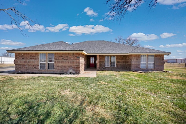 view of front of property featuring roof with shingles, a front lawn, and brick siding