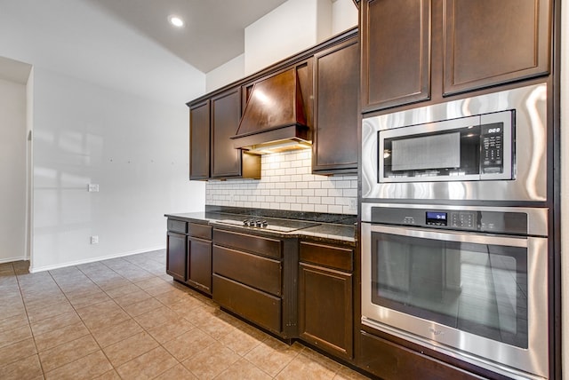 504 Wagner, Midland, TX 79706 - kitchen featuring appliances with stainless steel finishes, decorative backsplash, dark brown cabinetry, light tile patterned floors, and custom range hood