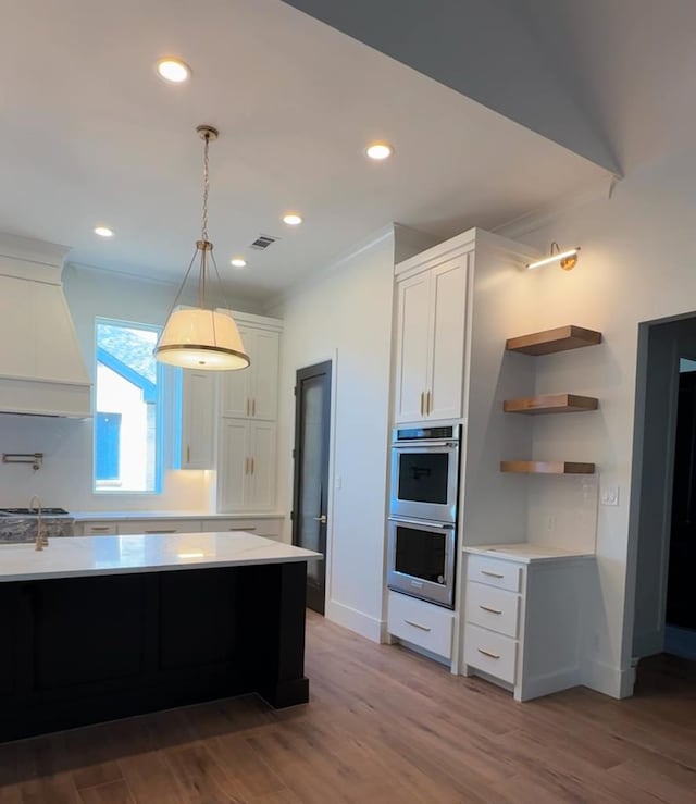 kitchen featuring white cabinetry, hanging light fixtures, stainless steel double oven, hardwood / wood-style floors, and custom exhaust hood