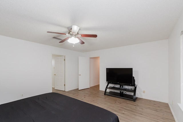 bedroom with a textured ceiling, light wood-style floors, baseboards, and ceiling fan