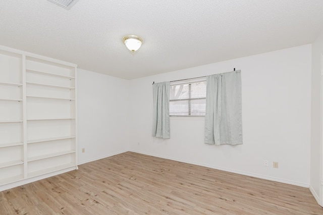 empty room featuring visible vents, a textured ceiling, baseboards, and wood finished floors