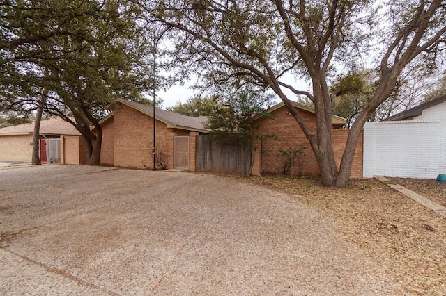 view of front of home featuring brick siding, driveway, and fence