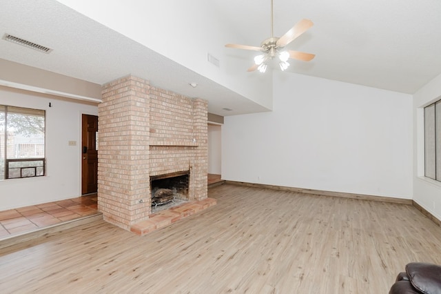 unfurnished living room featuring vaulted ceiling, a textured ceiling, ceiling fan, a fireplace, and light hardwood / wood-style floors