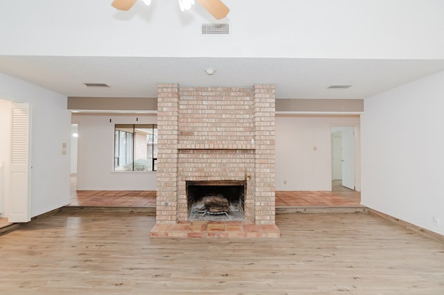 unfurnished living room featuring a ceiling fan, a brick fireplace, wood finished floors, and visible vents