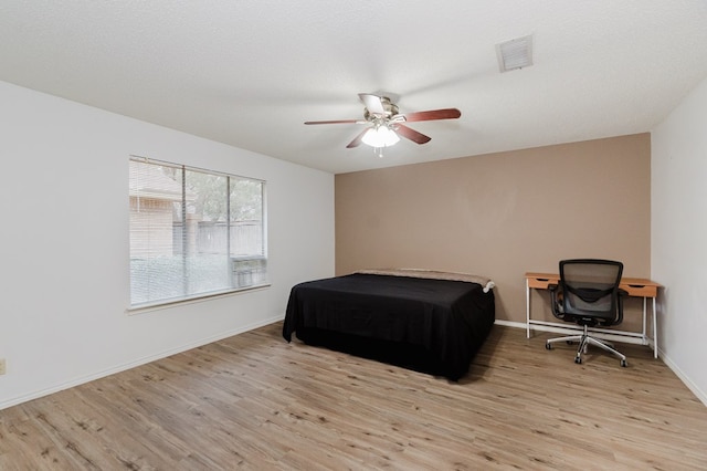 bedroom with visible vents, baseboards, wood finished floors, a textured ceiling, and a ceiling fan